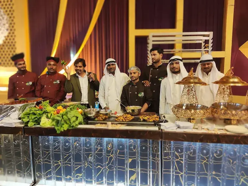 The team behind a live catering counter, plating to order beside covered service dishes.