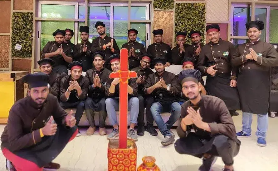 The team assembled indoors at the close of a banquet, hands folded in greeting.